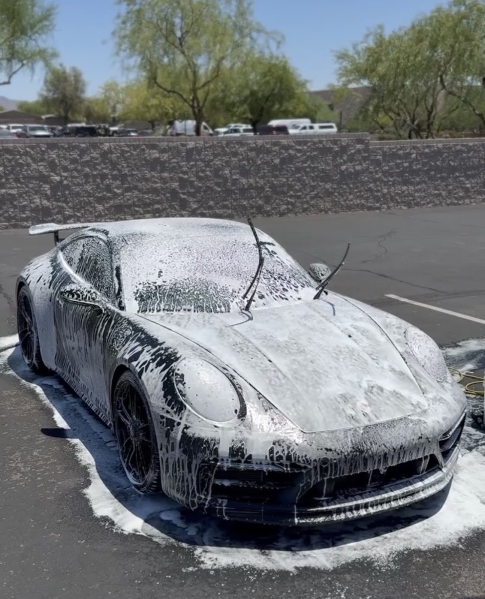 Cascading foam on a black Porsche 911, mid-foam, sunlit